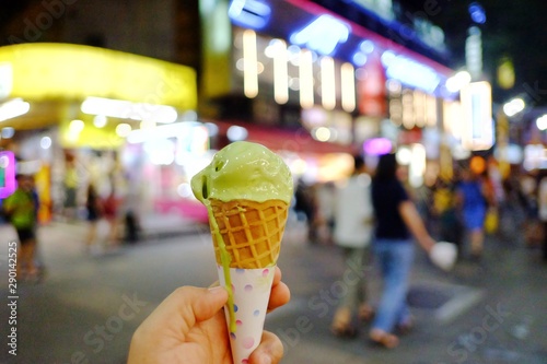 A female hand holding a melting green tea ice cream cone with a view at night market in Ximending,Taipei,Taiwan