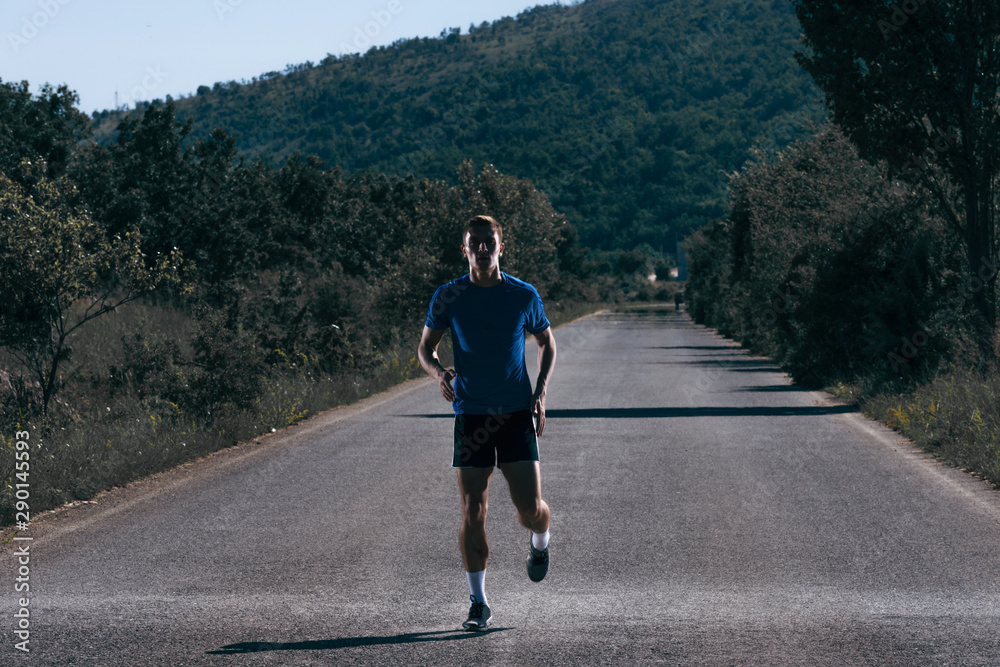 Fototapeta premium Male athlete running on an empty road in the woods while trying to get to the red finish line.