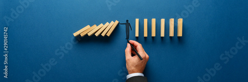 Silhouette of a man making a stop gesture to prevent wooden dominos from collapsing photo