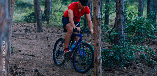 Fit cyclist riding his bike downhill through a forest ( woods ) while wearing a red shirt and red shoes.