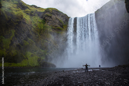 skógafoss, Iceland »; August 2017: A young man under the waterfall with open arms and his beautiful surroundings