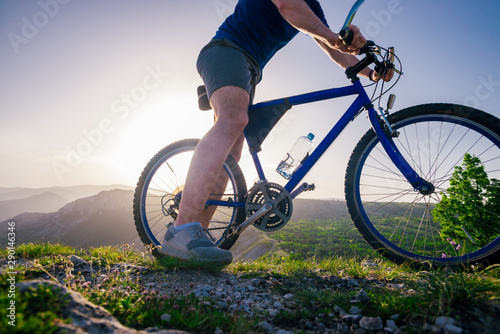 Close up photo from a mountain biker riding his bike ( bicycle) on rough rocky terrain on top of a mountain, wearing no safety equipment. Adrenalin junkie.