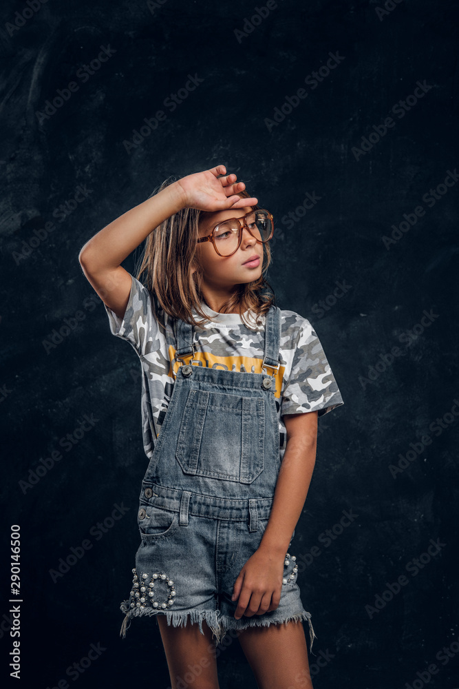 Cute girl in big glasses is posing for photographer at dark photo studio.