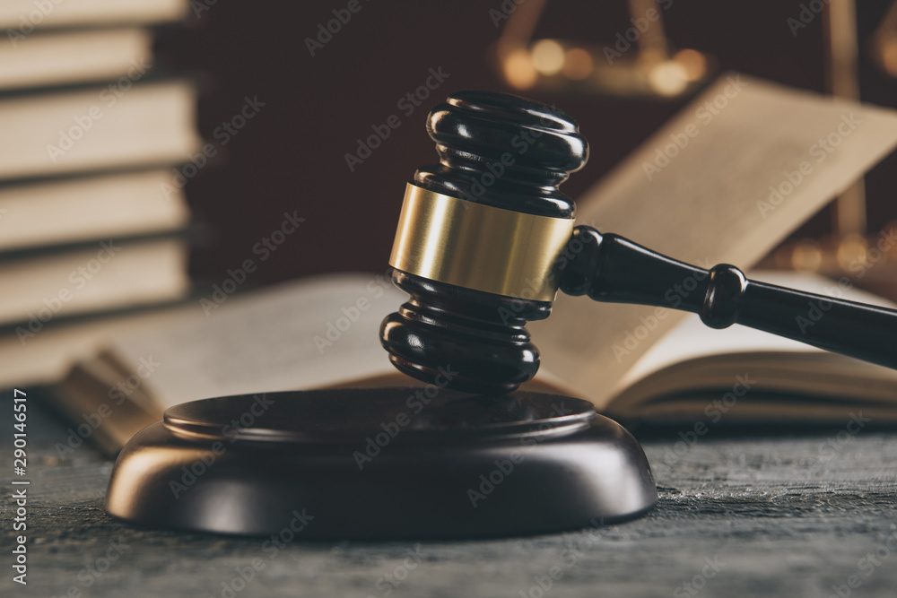 Law concept - Open law book with a wooden judges gavel on table in a courtroom or law enforcement office on black background.