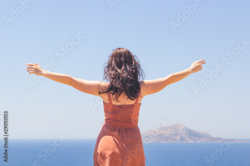 Young girl in dress looking at blue seascape and enjoying summer vacation
