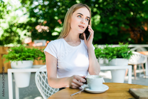 Young charming woman calling with cell telephone while sitting alone in coffee shop during free time. Attractive female with cute smile having talking conversation with mobile phone while rest in cafe
