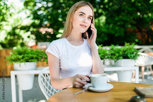 Young charming woman calling with cell telephone while sitting alone in coffee shop during free time. Attractive female with cute smile having talking conversation with mobile phone while rest in cafe