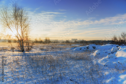 Winter landscape. Frozen field on a background of sunset, cityscape and tower crane. Bright clouds.
