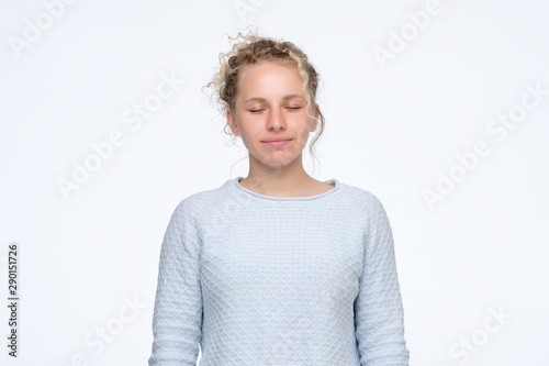 Calm young caucasian girl with curly hair standing with closed eyes with slight smile. Studio shot