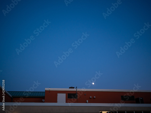 moon peeking above a building on a fall evening