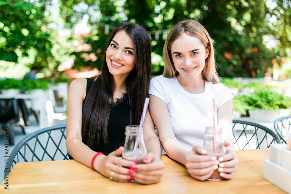 Portrait of cheerful young friends having fresh juice. Two young women at juice bar having a glass of fresh fruit juice together. Portrait of cheerful young friends having fresh juice. Two young women at juice bar having a glass of fresh fruit juice together.