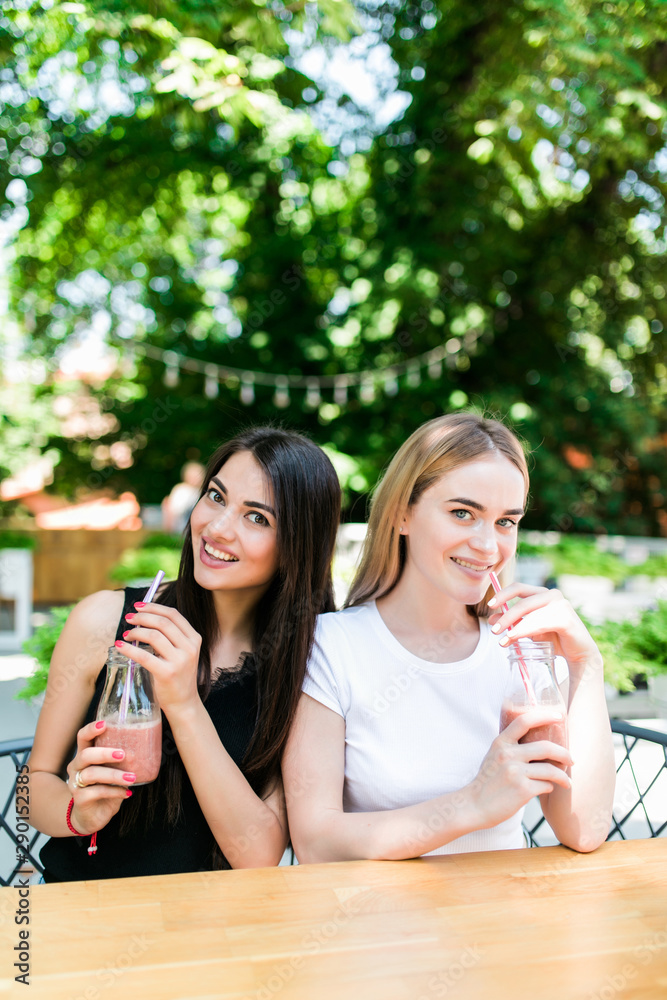 Portrait of cheerful young friends having fresh juice. Two young women at juice bar having a glass of fresh fruit juice together. Portrait of cheerful young friends having fresh juice. Two young women at juice bar having a glass of fresh fruit juice together.