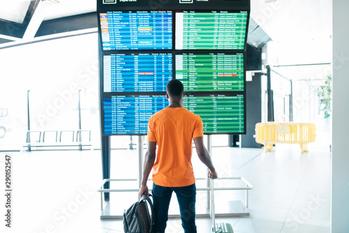 Rear view of man looking at arrival and departure board in airport