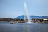 A beautiful rainbow colors the mist on the symbol of Geneva, a 140m water fountain on Lake Geneva called the Jet D'eau in front of a clear blue sky in Switzerland. Vertical copy space