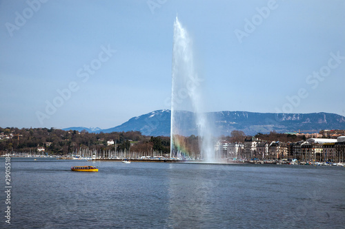 A beautiful rainbow colors the mist on the symbol of Geneva, a 140m water fountain on Lake Geneva called the Jet D'eau in front of a clear blue sky in Switzerland. Vertical copy space