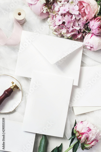 Feminine wedding, birthday mock-up scene. Blank craft paper greeting cards, peony, hydrangea, roses flowers, vintage seal stamp and silk ribbon. White table background. Vertical flat lay, top view