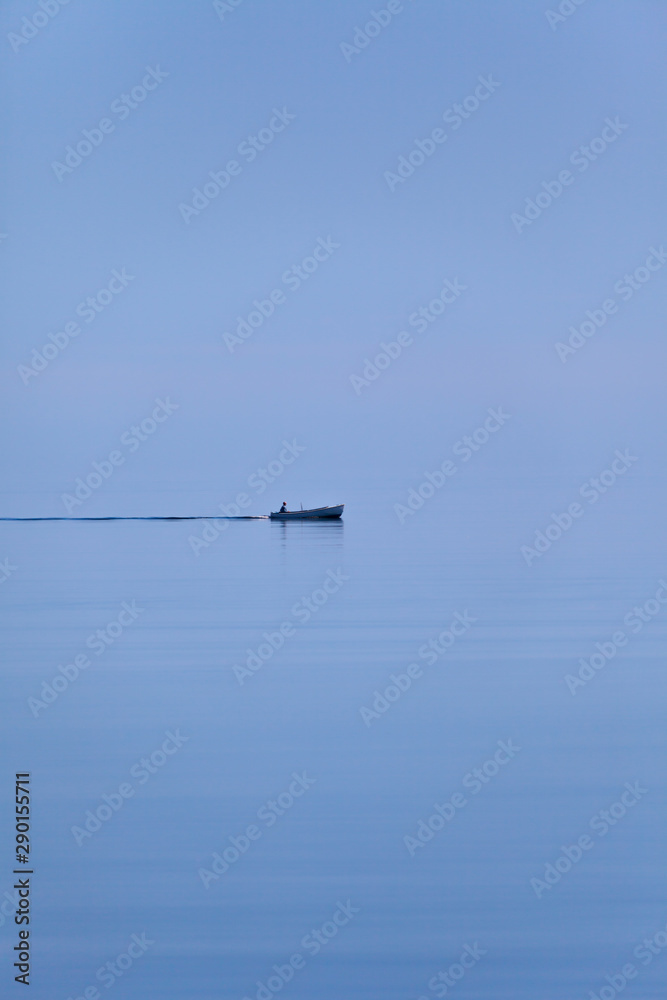 Calm sea and pale morning light. Lonely skiff. Sky and sea merge on the horizon. Calm sea and pale morning light. Lonely skiff. Sky and sea merge on the horizon.