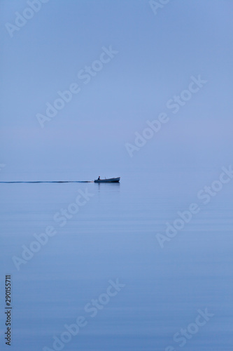 Calm sea and pale morning light. Lonely skiff. Sky and sea merge on the horizon.