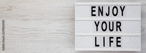 'Enjoy your life' words on a modern board over white wooden background, top view. Overhead, from above. Flat lay. Copy space.