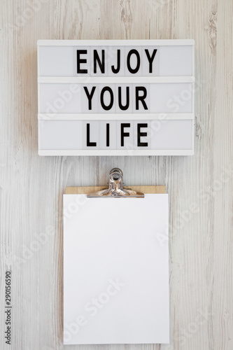 Lightbox with text 'Enjoy your life', noticepad with blank sheet of paper on a white wooden background, top view. Overhead, from above. Flat lay. Space for text. photo