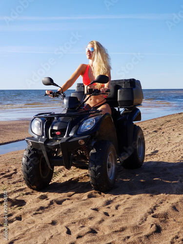 attractive woman in bikini with long blonde hair is sitting on the quad bike, sunny day.