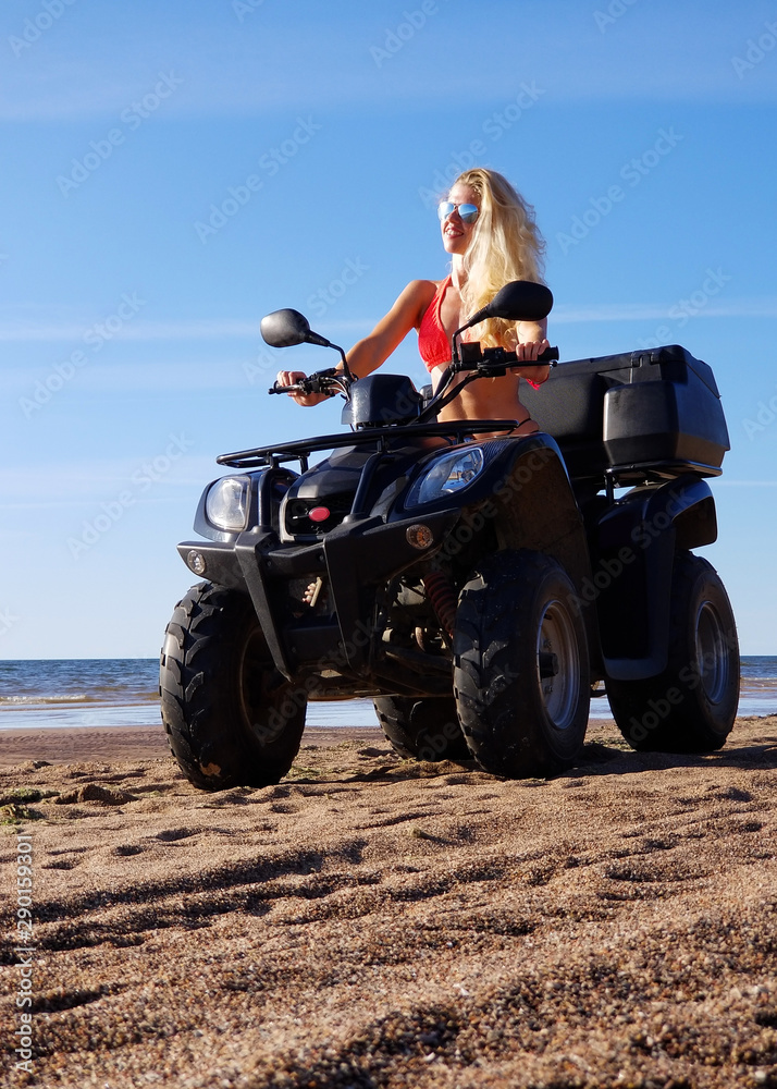 attractive woman in bikini with long blonde hair is sitting on the quad bike, sunny day.
