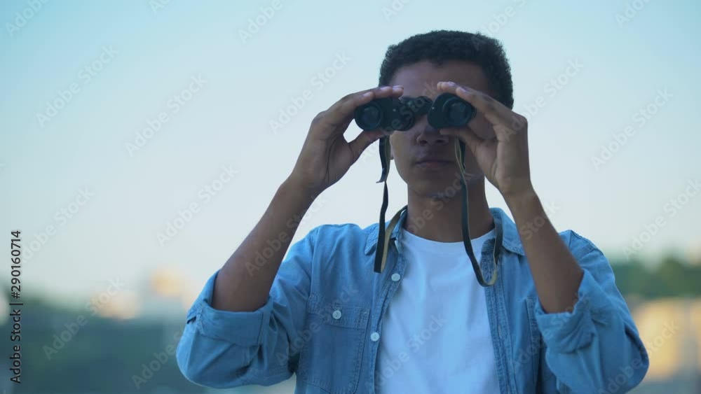 Mixed-race guy looking at skyline with binoculars, dreaming to be sailor
