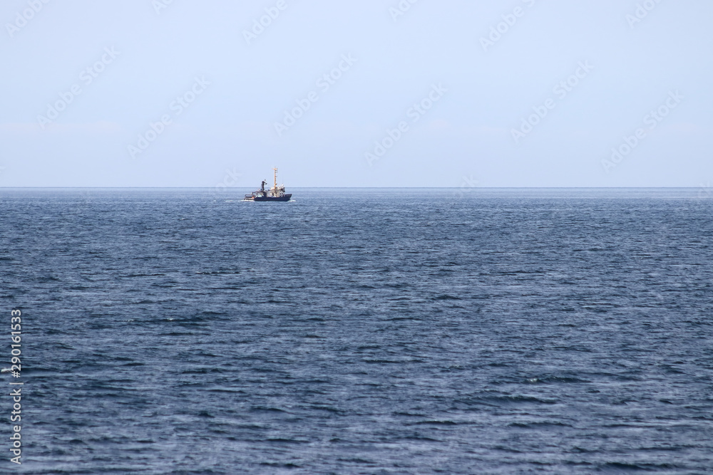 Fishing boat on horizon underway departing to the sea. Background, template, wallpaper.