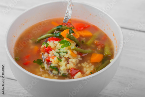 Vegetable soup in a ceramic bowl is mixed with a spoon