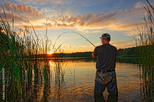 Angler catching the fish in the lake during summer sunset
