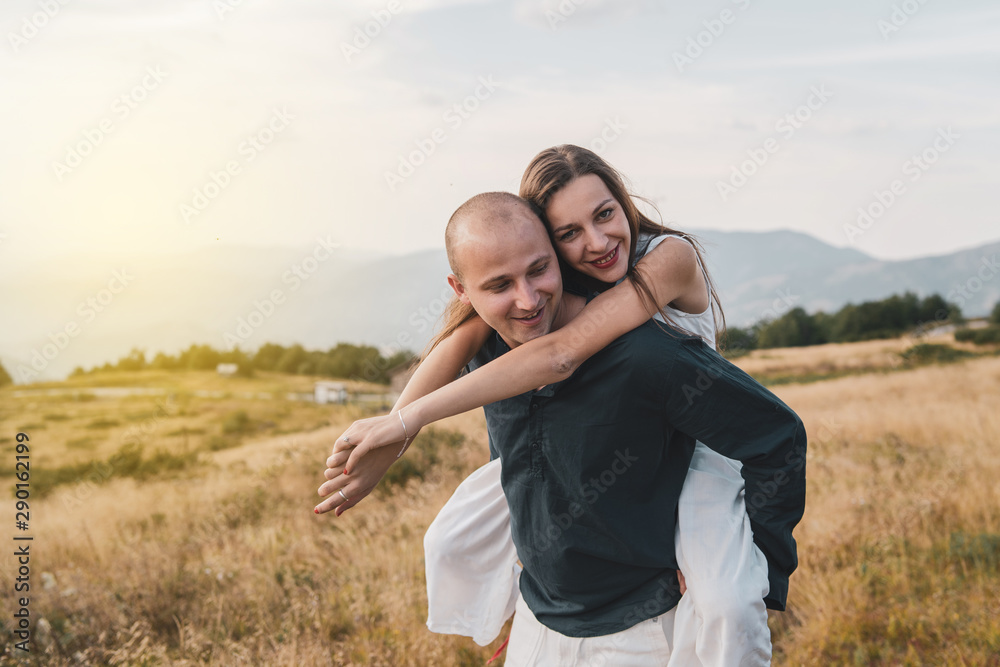 Young couple married in love man and woman young girl boyfriend husband is holding her on the mountain range in nature in summer or autumn day while she hug him from the back Young couple married in love man and woman young girl boyfriend husband is holding her on the mountain range in nature in summer or autumn day while she hug him from the back