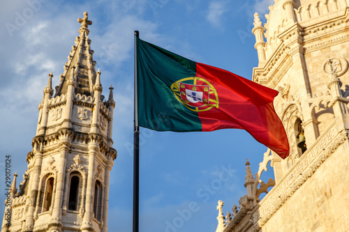 Obraz na plátně Portuguese flag waving in front of a blue sky and monastery.
