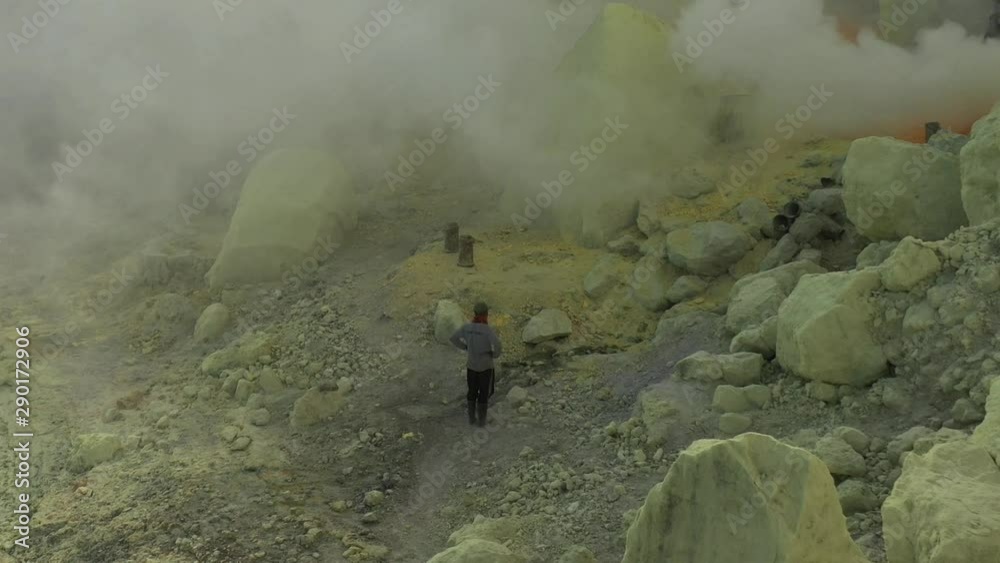 Aerial view of a sulfur miner avoids toxic sulfur gas clouds at the crater of Kawah Ijen volcano, East Java, Indonesia. Aerial view of a sulfur miner avoids toxic sulfur gas clouds at the crater of Kawah Ijen volcano, East Java, Indonesia.