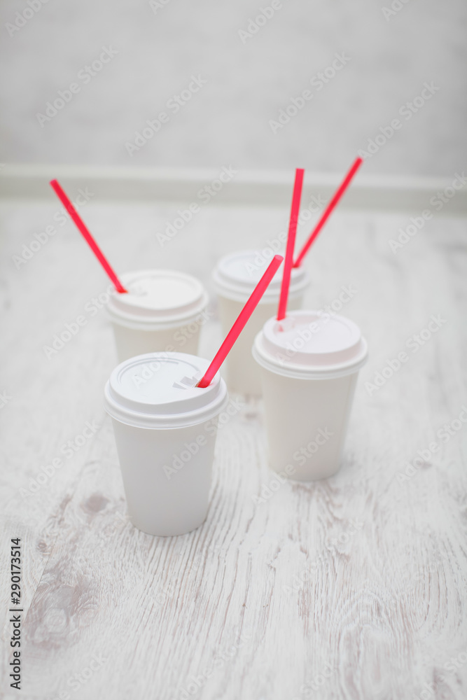 four white paper cups with red tubes for coffee to go on white wooden table in selective focus. four white paper cups with red tubes for coffee to go on white wooden table in selective focus.
