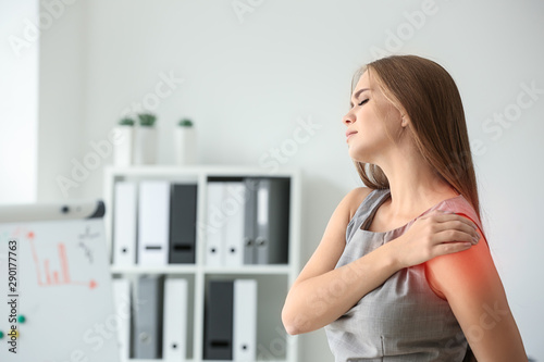 Young woman suffering from pain in shoulder at workplace