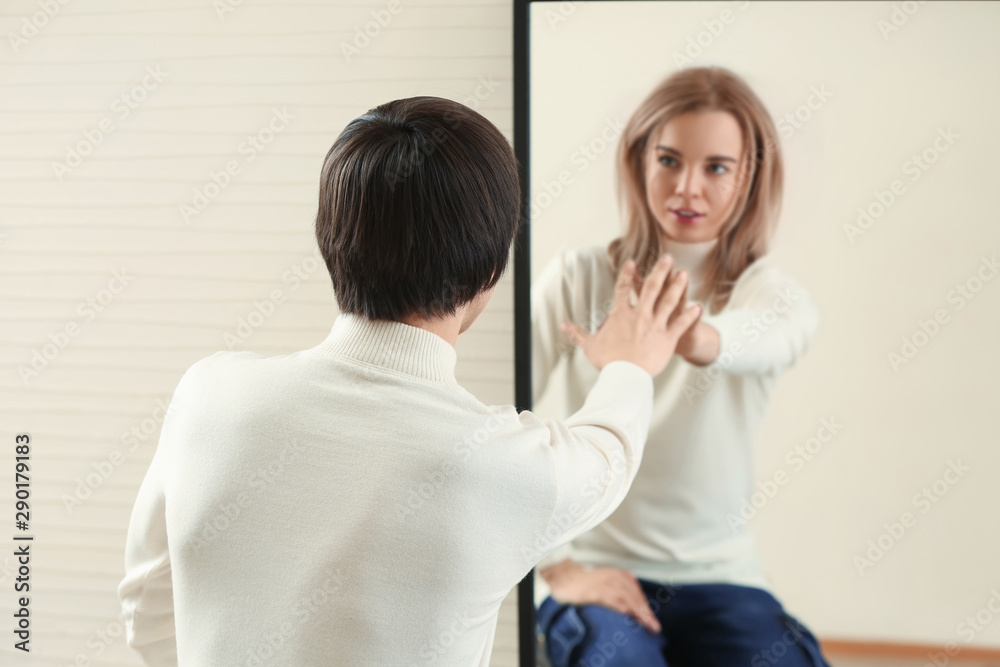 Young man looking at his imaginary reflection in mirror. Concept of transgenderism