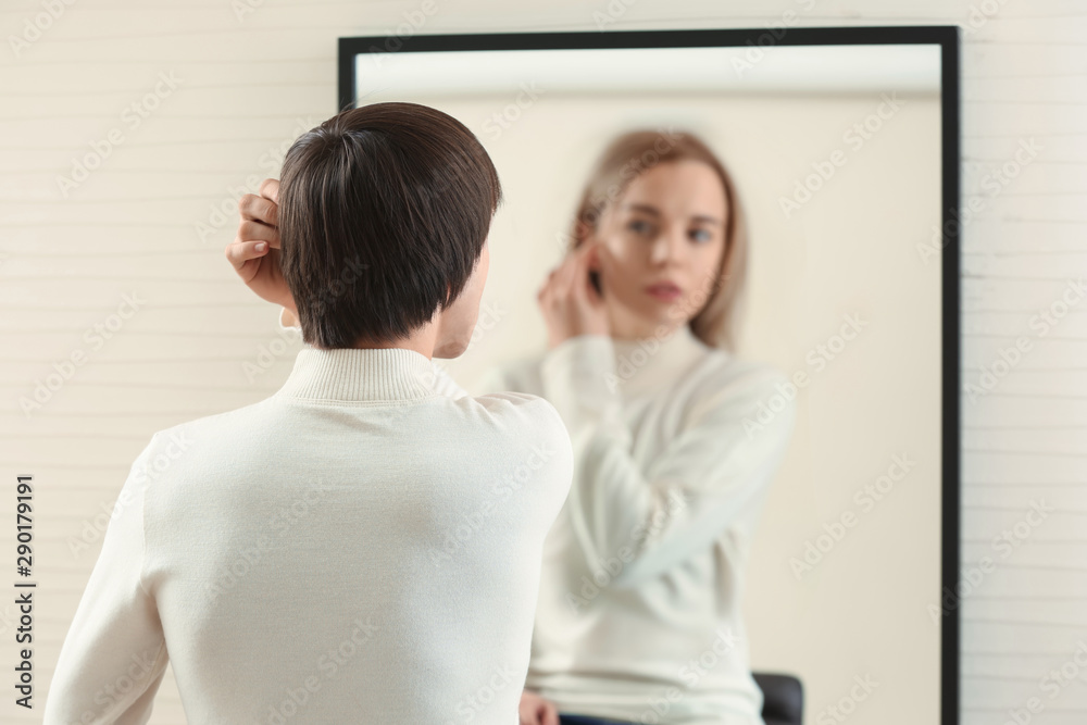 Young man looking at his imaginary reflection in mirror. Concept of transgenderism Young man looking at his imaginary reflection in mirror. Concept of transgenderism