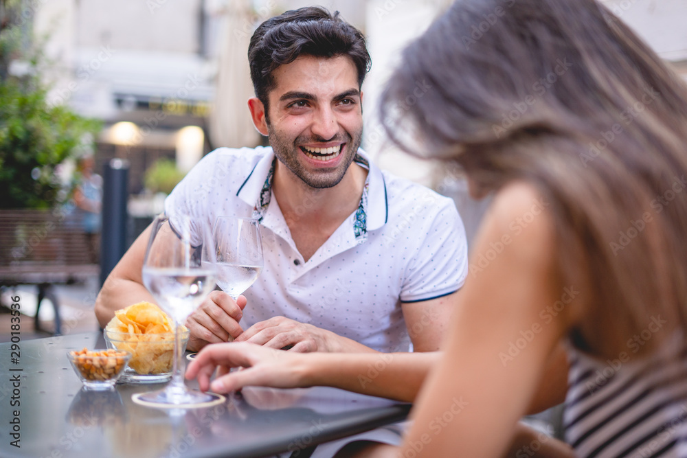Young man flirting with a woman, lifestyle concept of young people drinking white wine and relaxing during a date in a wine bar outdoors. Leisure lifestyle concept. Young man flirting with a woman, lifestyle concept of young people drinking white wine and relaxing during a date in a wine bar outdoors. Leisure lifestyle concept.