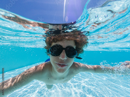 Little guy wearing goggles swimming underwater in a pool in the summer.