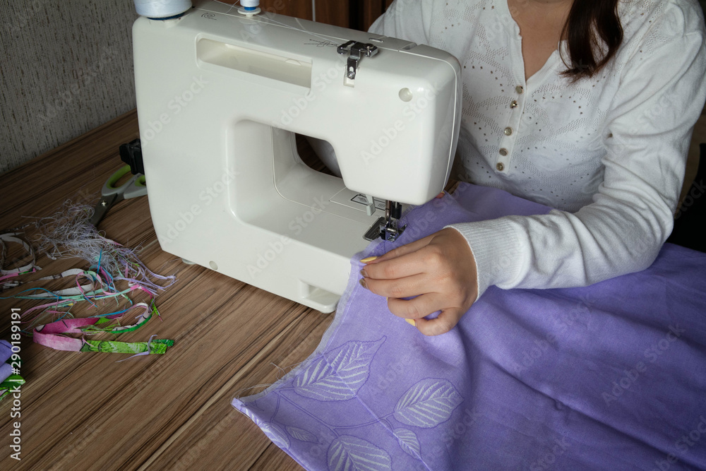 A woman sews a textile product at home on a sewing machine. Production of bed linen. Work at home.