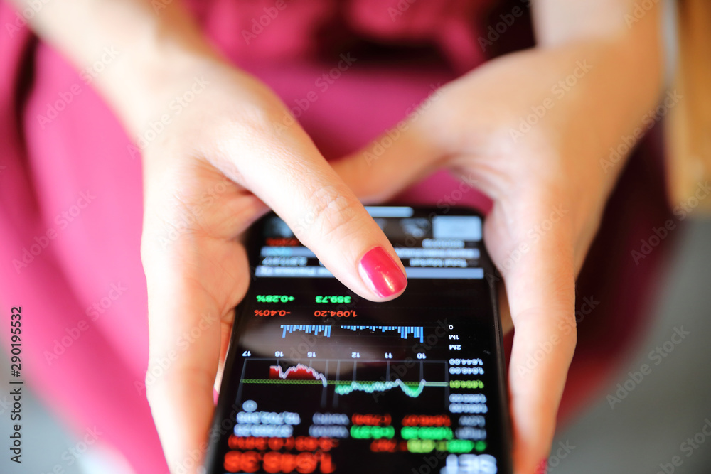 Female hand with smartphone trading stock online in coffee shop , Business concept Female hand with smartphone trading stock online in coffee shop , Business concept