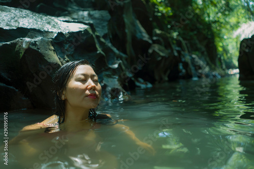happy Asian Chinese woman in bikini enjoying unique Summer holidays at tropical forest refreshing relaxed in natural pool delighted by the magical feeling at the jungle lake