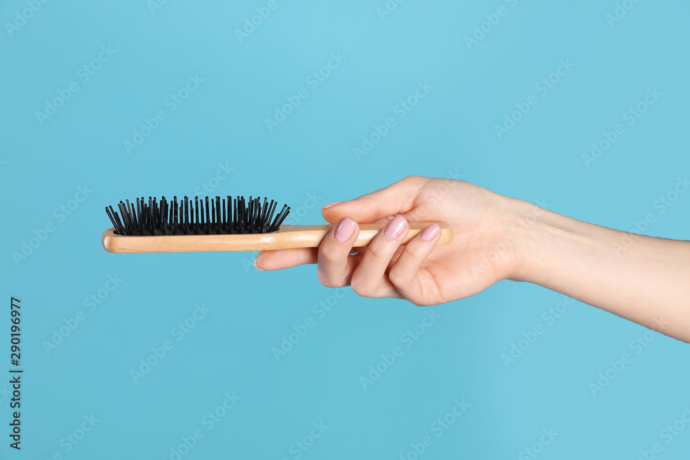 Naklejka premium Woman holding wooden hair brush against blue background, closeup
