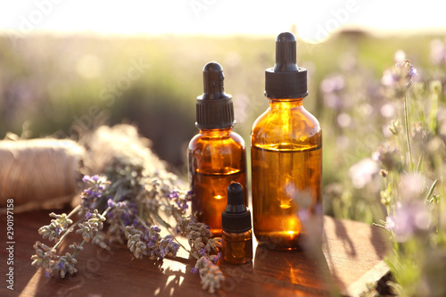 Bottles of lavender essential oil on wooden table in field