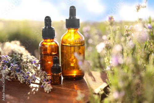 Bottles of lavender essential oil on wooden table in field. Space for text