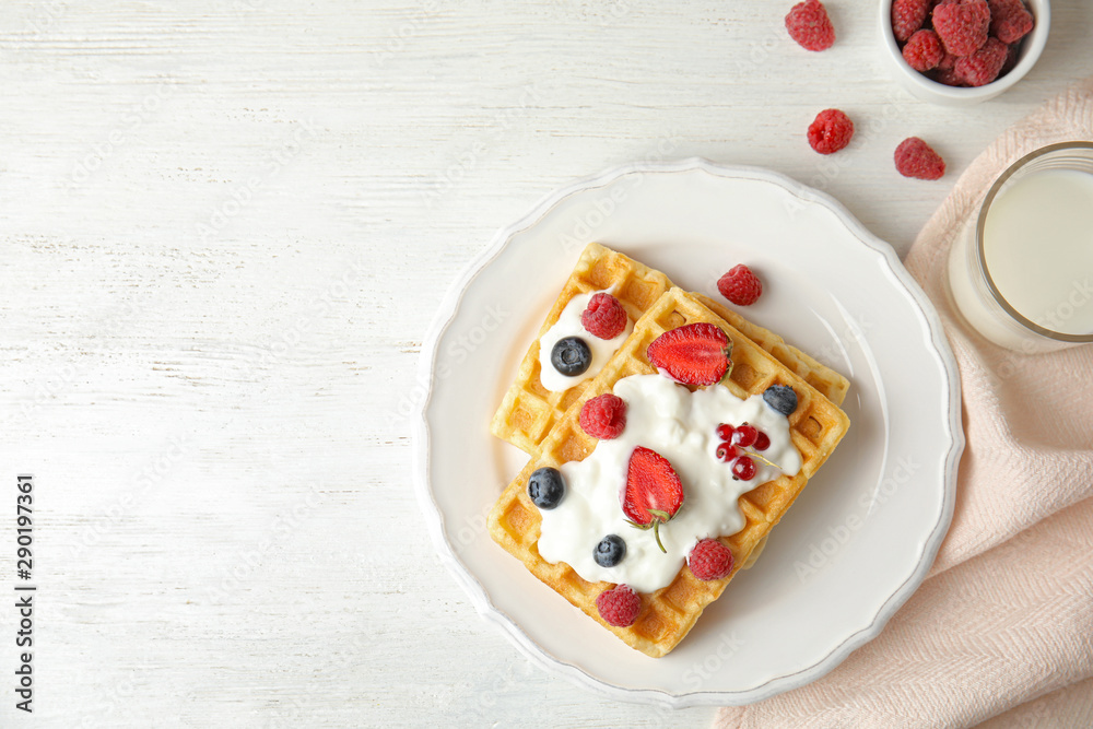 Flat lay composition with delicious waffles and fresh berries on white wooden table. Space for text