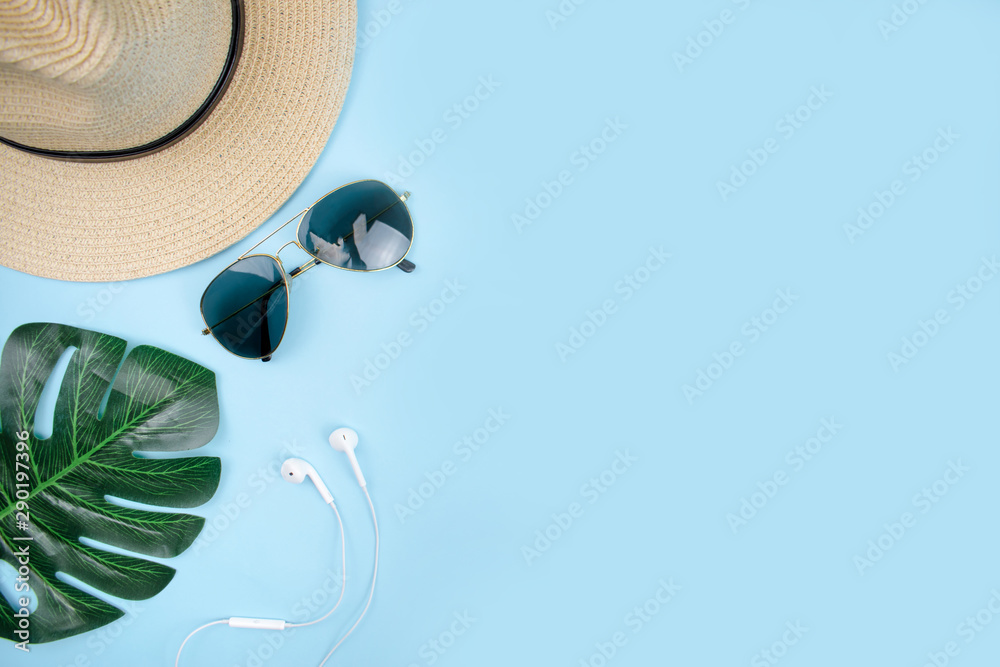 Top view of travel accessories with sun glasses, hat, and leaves on a blue background. - obrazy, fototapety, plakaty 
