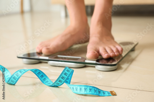 Tape in front of woman standing on floor scales indoors. Overweight problem photo