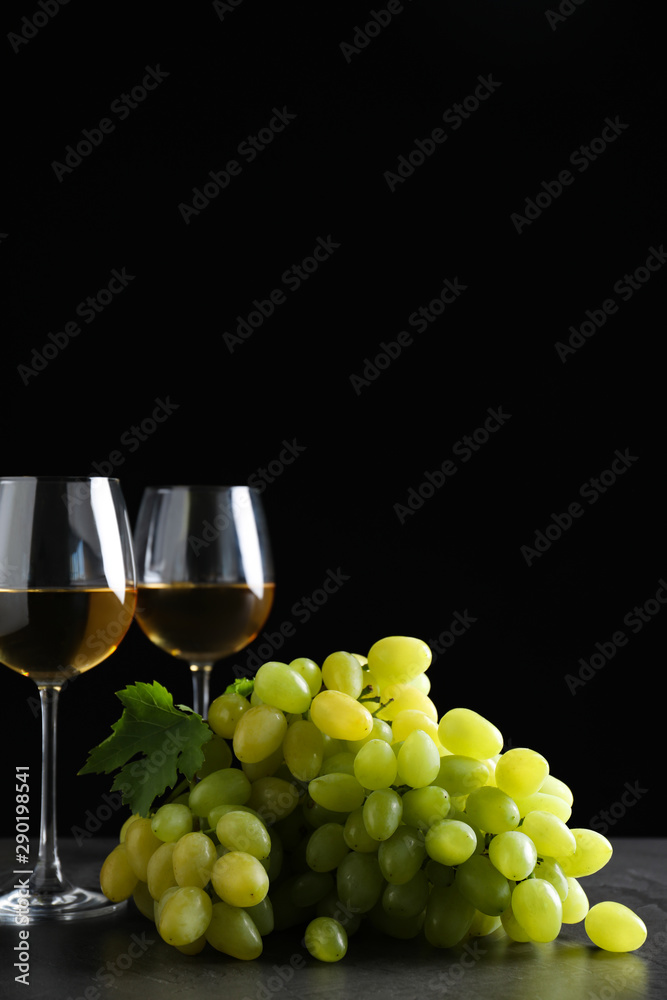Fresh ripe juicy grapes with wineglasses on grey table against black background, space for text
