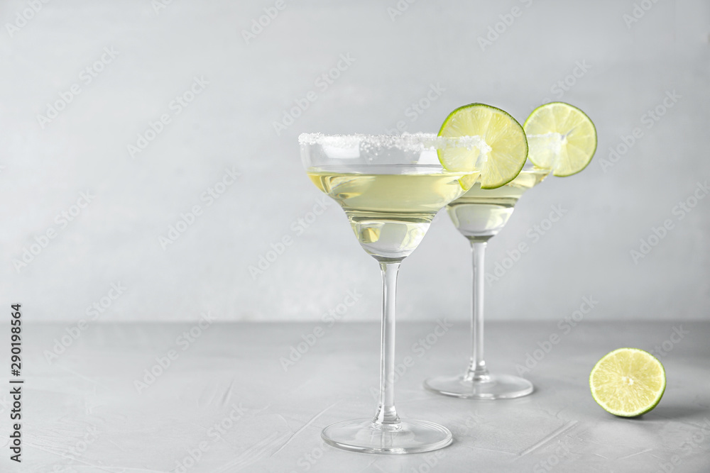 Glasses of lemon drop martini cocktail with lime slice on light table against grey background. Space for text